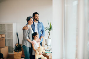 Happy parents with daughter enjoying at their new house and looking through the window. Copy space.